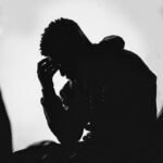 man in black hoodie covering his face with his hands